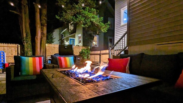 An outdoor patio with a fire feature, wooden furniture, and a view of neighboring houses.