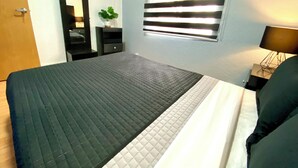 A bedroom with a bed, a dresser, a mirror, a window with blinds, and a bedside lamp. - RMS Hostal - WTC (Mexico City)