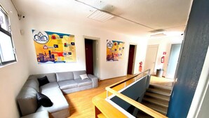 A modern interior with a grey sectional sofa, wooden flooring, and a staircase with a metal handrail. - RMS Hostal - WTC (Mexico City)