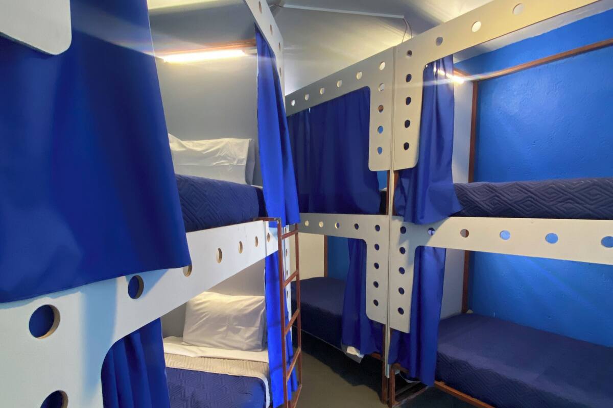 A narrow corridor with bunk beds, blue curtains, and a ceiling light.