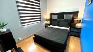 A bedroom with a bed, bedside tables, a lamp, a potted plant, and a window with blinds. - RMS Hostal - WTC (Mexico City)