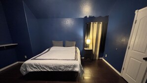 A bedroom with a bed, a nightstand, a lamp, a door, and a blue wall. - Efficient and Modern home, Sleeps 8. Theres an airmattress that sleeps 2. (Oklahoma City)