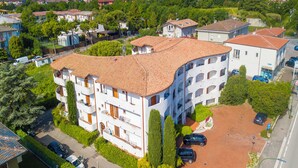 Un immeuble à plusieurs étages, doté d’un toit incurvé, entouré de verdure et de voitures garées.