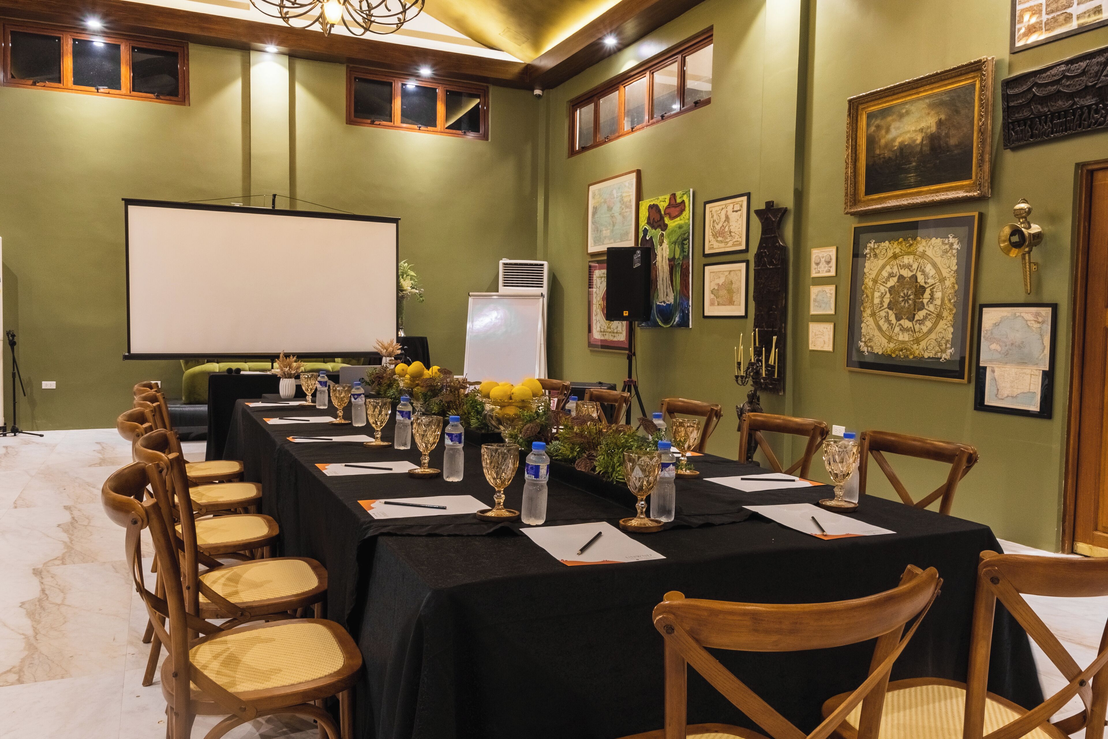 A conference room with a long table, chairs, a projector screen, and framed artwork on the walls.