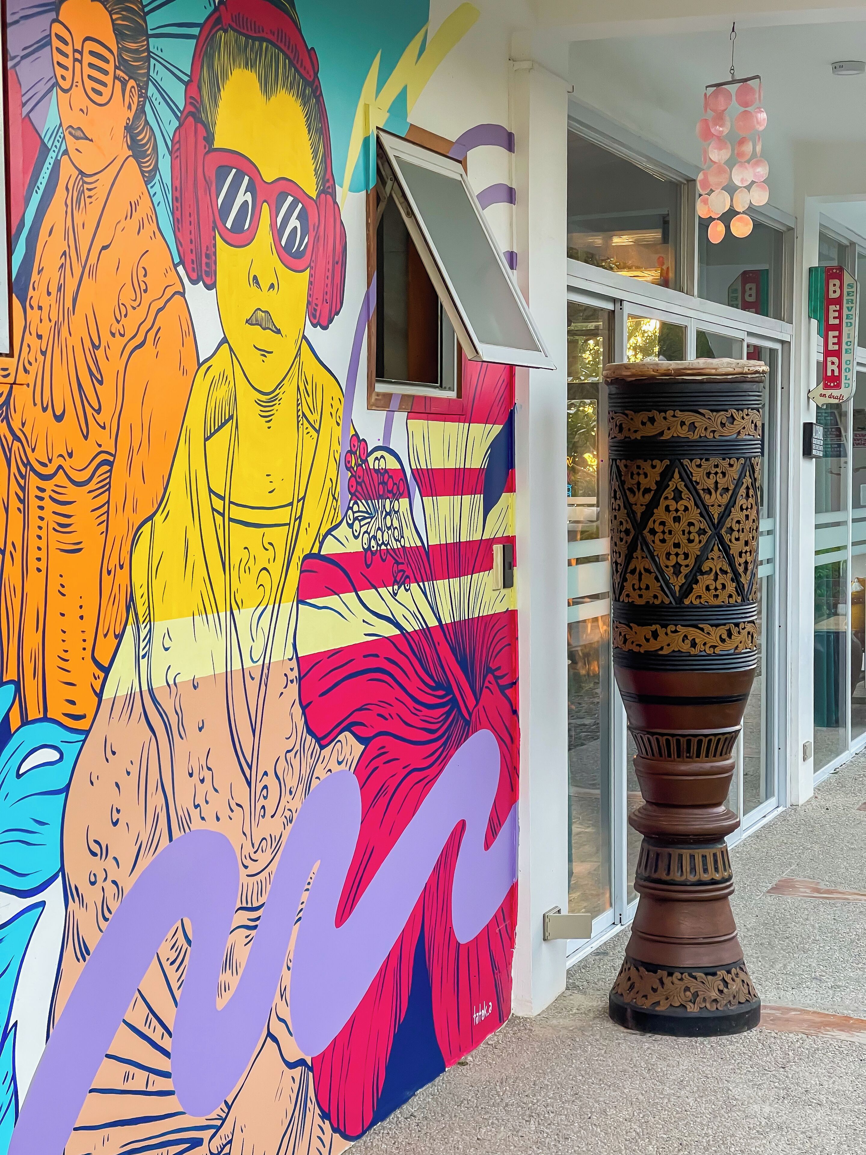 A colorful mural with abstract figures and a decorative column outside a building.