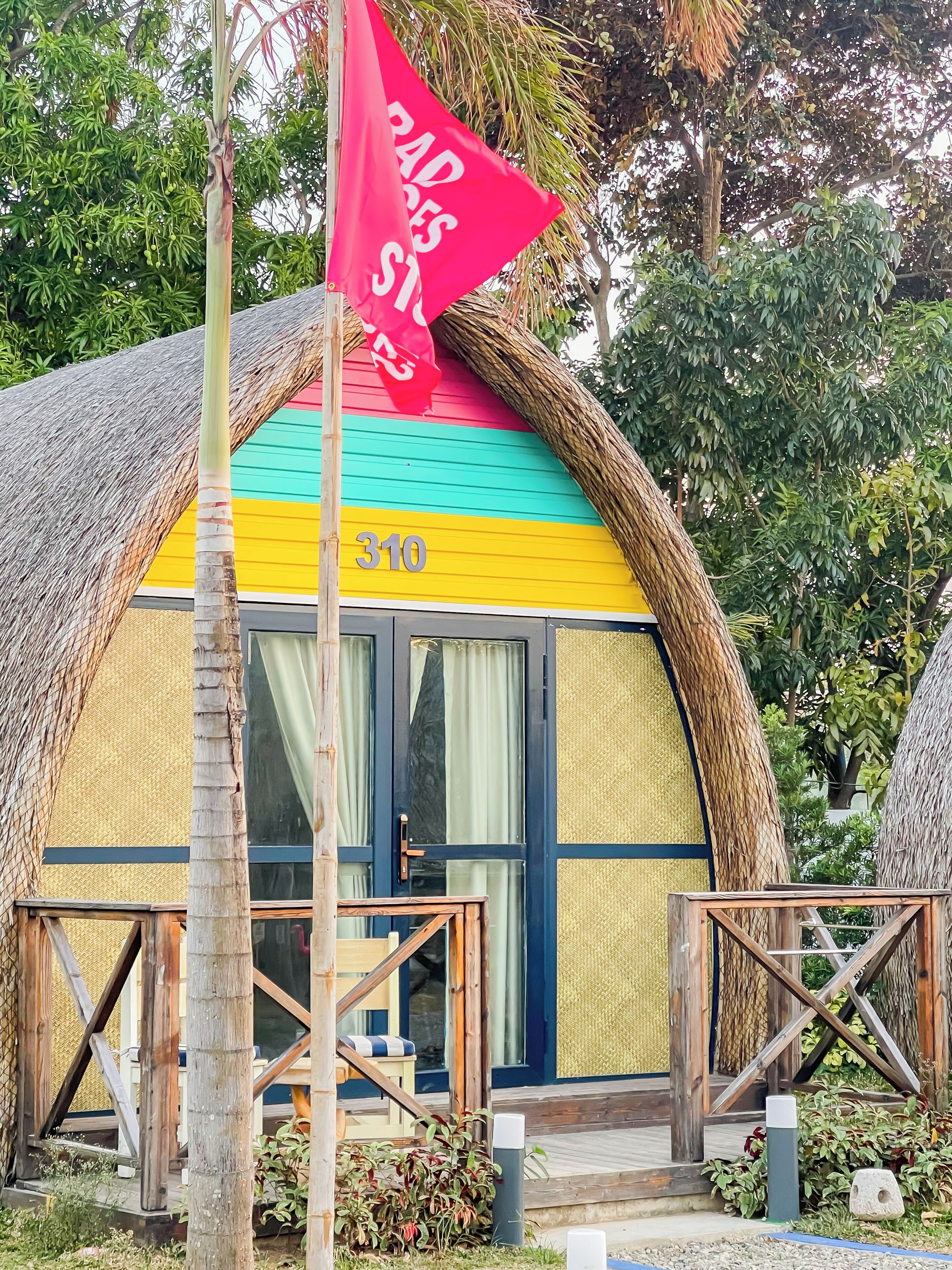 A thatched-roof building with a colorful exterior, a flag, and a number '310' sign.