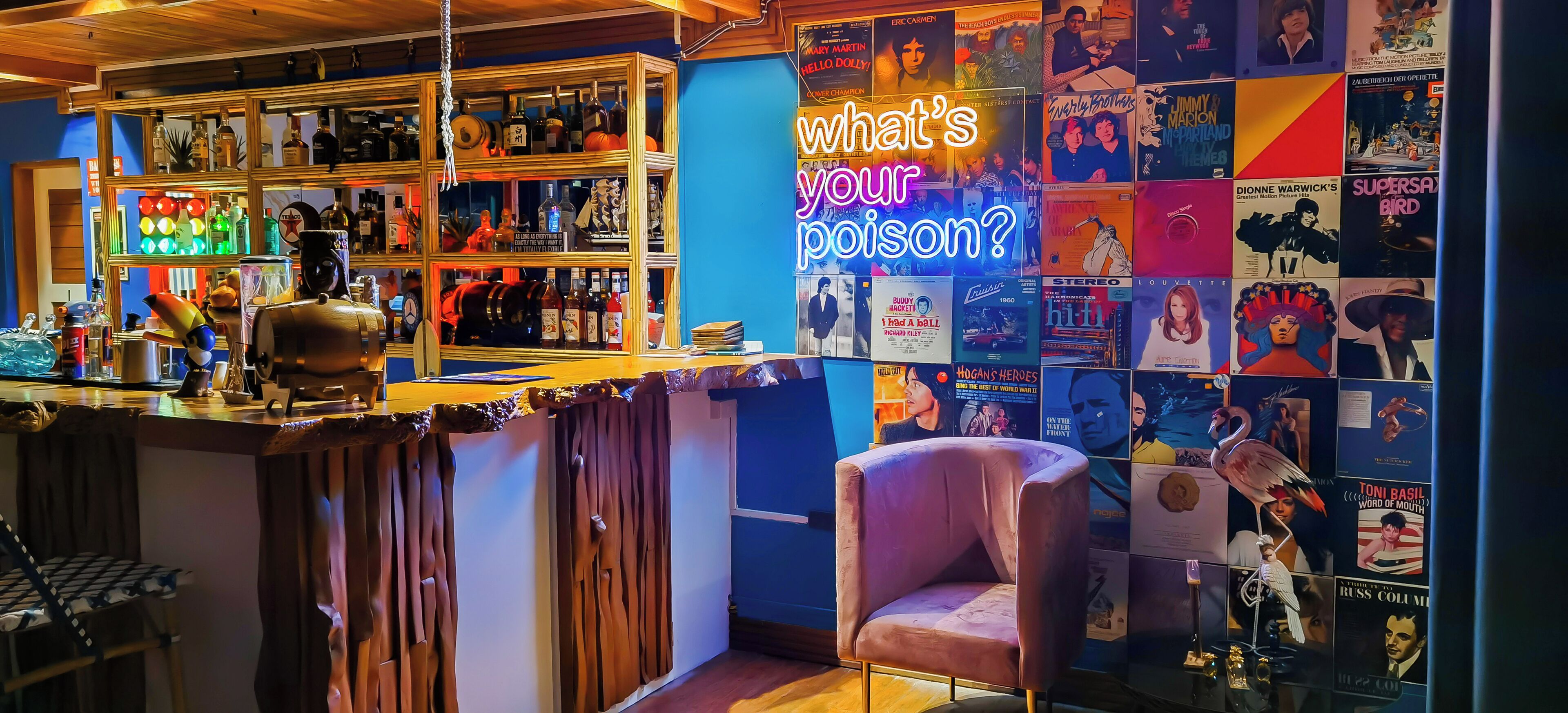 Een bar met flessen op de planken en een neonbord waarop staat: 'Wat is je drankje?'