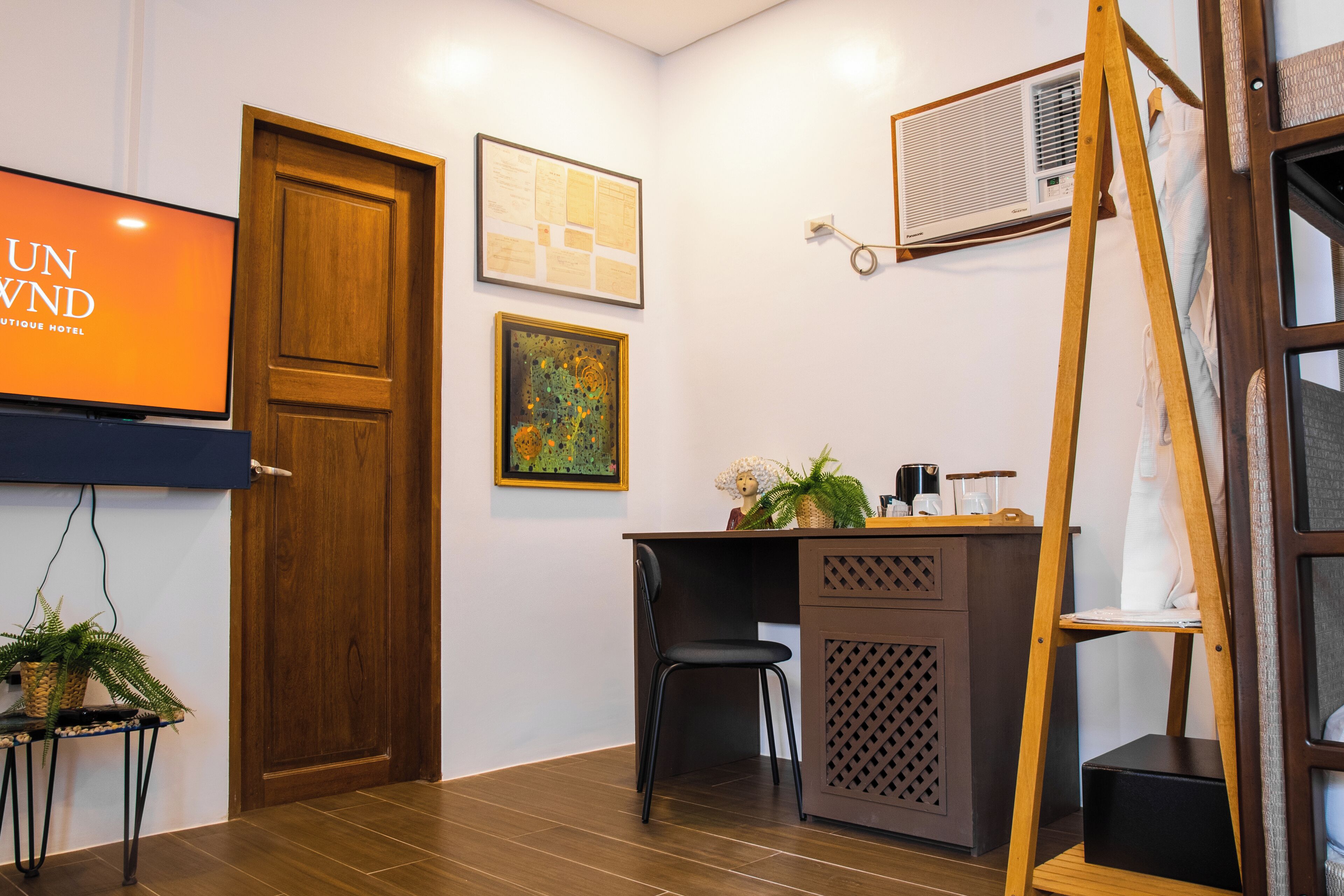 Una camera d'albergo con una porta in legno, una scrivania con una sedia, una televisione e un condizionatore d'aria fissato al muro.