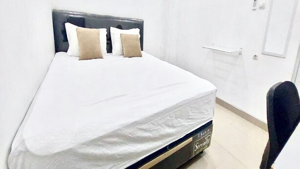 A neatly made bed with a white mattress and two pillows, a dark headboard, and a white door with a handle. - Hotel O Homestay Pak To Syariah (Surabaya)