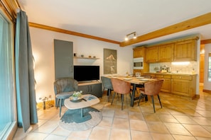 A modern living room with a TV, seating, and a dining area with a table and chairs.