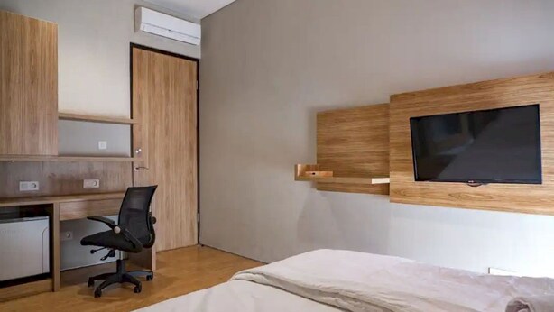 A bedroom with a bed, a desk with a chair, a TV mounted on the wall, and a wardrobe.