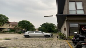 A parking area with a white car and a motorcycle, a building with a sign, and trees in the background.