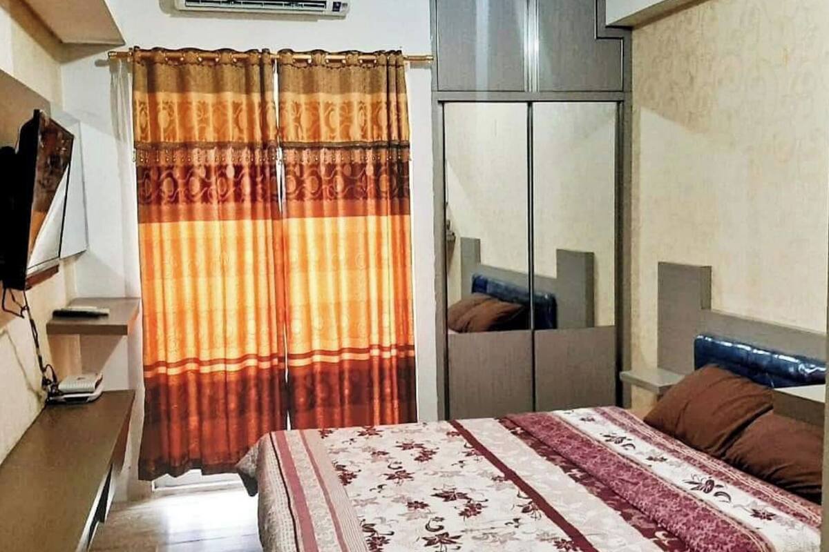 Un dormitorio con una cama, un armario, un equipo de aire acondicionado y un televisor sobre un escritorio.