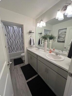 Un baño moderno con dos lavamanos, un inodoro, una ducha y un espejo grande.