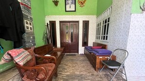 Una habitación con un sofá de madera, una pequeña mesa de madera, una silla plegable de metal y una puerta con un cuadro enmarcado encima.