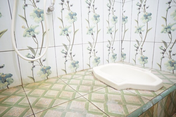 A bathroom with floral wall tiles, a shower hose, and a green patterned floor.