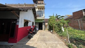 Un callejón estrecho con un edificio de fachada roja y blanca, un pequeño balcón y una motocicleta estacionada al frente.