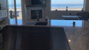Eine Küche mit großem Fenster zum Strand, einem flachbildfernseher über der Spüle und einem Kamin.