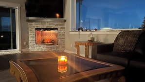 Ein Wohnzimmer mit Kamin, einem darüber montierten Fernseher und Blick durch ein großes Fenster.