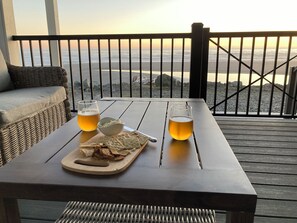 A table with a glass of beer, a bowl of chips, and a cutting board with bread on a wooden deck overlooking the ocean. - Prime Oceanfront Getaway.  Beach access. AC, Fireplace. EV Charger, Pet Free. (Gold Beach)