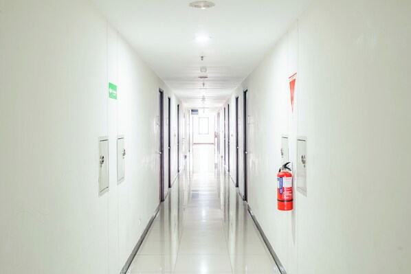 Un pasillo largo y estrecho con puertas a ambos lados, un extintor en la pared y una luz en el techo.