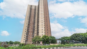Un edificio residencial alto con varios pisos y balcones, rodeado de follaje y un cielo despejado.