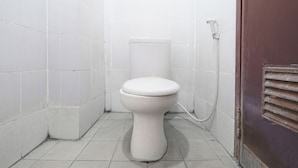Un inodoro pequeño y blanco en un rincón de un baño con paredes y suelo de baldosas blancas.