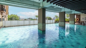 Una piscina interior con agua azul cristalina, sostenida por columnas, y vista del paisaje urbano a través de un techo de vidrio.