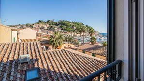 Un pueblo costero con tejados de teja terracota, un puerto deportivo y edificios en una colina.