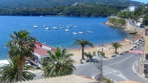 Vista costera con barcos en el agua, palmeras y una carretera con edificios.