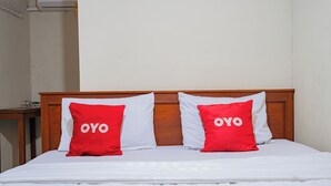 Een bed met een houten hoofdbord, twee rode kussens met de tekst 'OYO' en een witte dekbedovertrek.