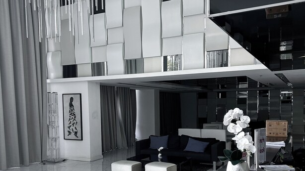 A modern living room with a high ceiling, a sofa set, a coffee table, and a decorative vase with flowers. - Vision condo (Pattaya)