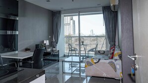 A modern living room with a sofa, dining table, chairs, and a balcony with a view of buildings. - Vision condo (Pattaya)