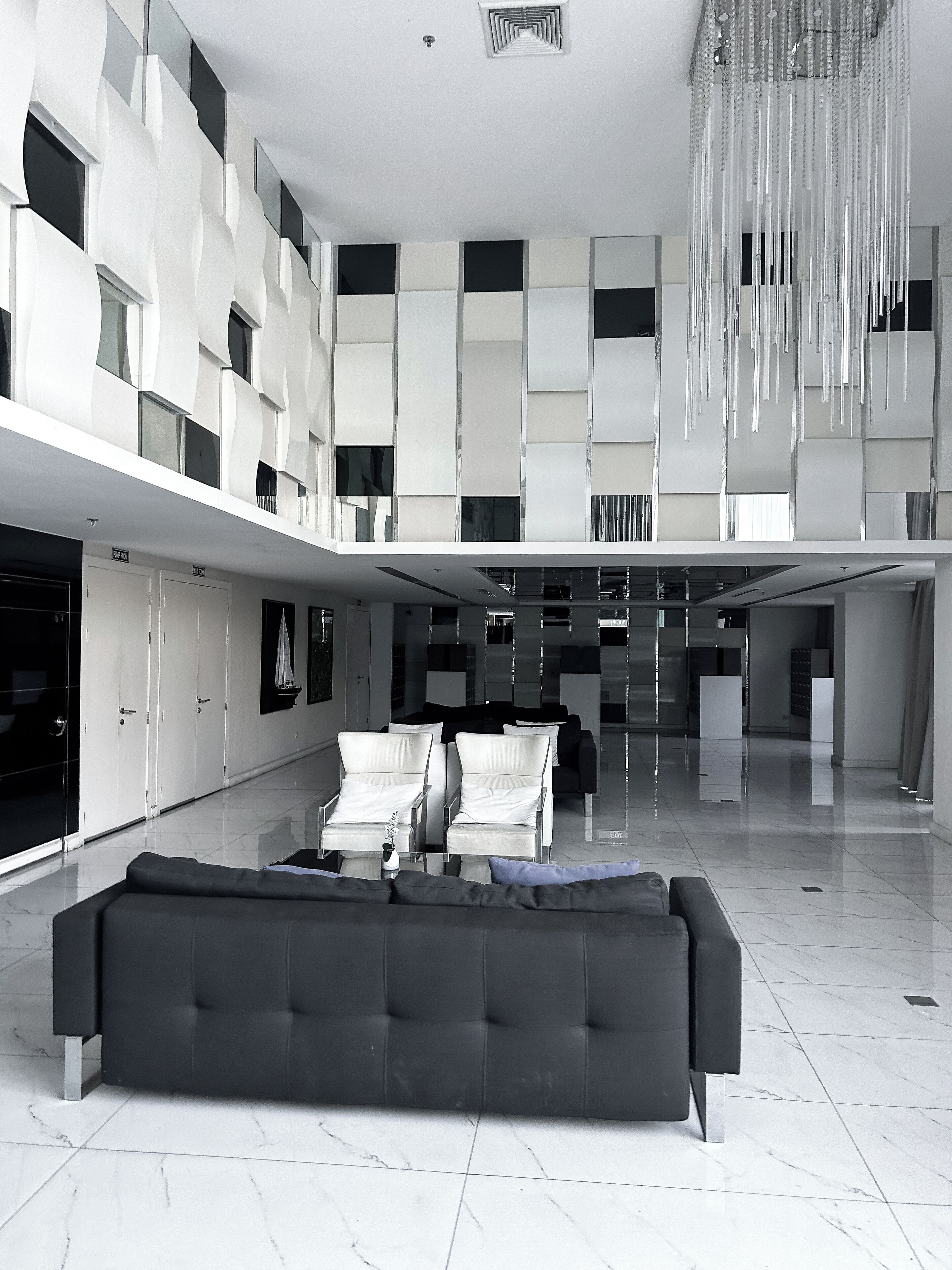Un'ampia hall dal design moderno, con un grande divano nero, diverse zone relax e un soffitto alto impreziosito da un lampadario particolare.