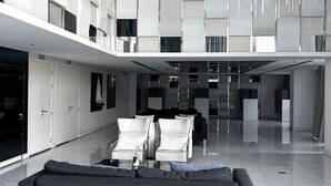 A spacious lobby with a modern design, featuring a large black sofa, multiple seating areas, and a high ceiling with a unique light fixture. - Vision condo (Pattaya)