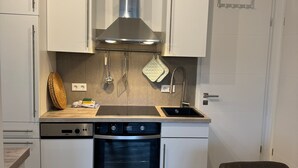 Een kleine keuken met witte kastjes, een roestvrijstalen afzuigkap, een vaatwasser en een oven.