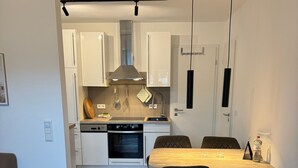Een moderne keuken met witte kastjes, een ingebouwde oven en een eethoek met een houten tafel en stoelen.