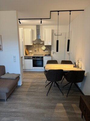 A modern kitchen with white cabinets, a built-in oven, and a dining area with a wooden table and chairs. - Apartment 'Residenz Lindengarten - Wohnung 16' with Private Terrace, Balcony and Wi-Fi (Kühlungsborn)