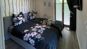 Un dormitorio con cama, televisión montada en la pared, lámpara en el techo y ventana con cortinas.