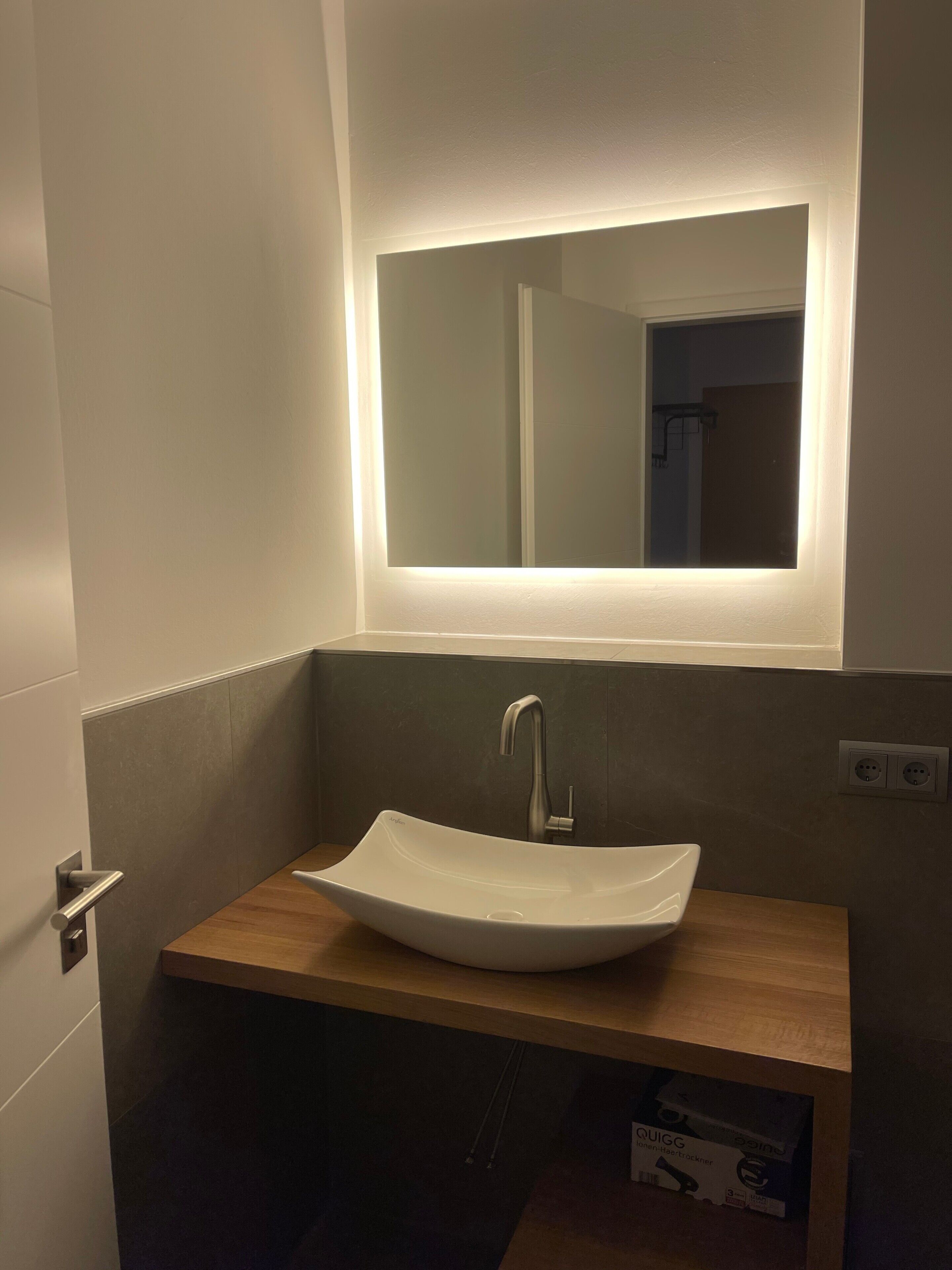 Ein Badezimmer mit einem weißen Waschtischbecken, einem modernen Wasserhahn und einem Spiegel mit integrierter Beleuchtung.