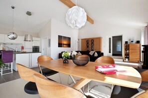 Une cuisine moderne avec des meubles blancs, un coin repas avec une table et des chaises en bois, et un salon avec un canapé et une cheminée.