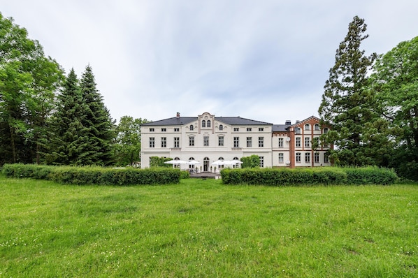 A large, historic building with a symmetrical facade, a central entrance, and a well-maintained lawn in front.