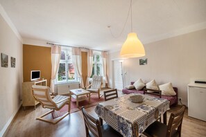 A cozy room with a dining table, chairs, a sofa, a TV, and a lamp.