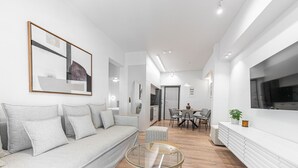 A modern living room with a grey sofa, a glass coffee table, and a dining area with a white table and chairs. - Phaedrus Living: Prosperity Residences Paradise (Athina)