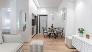 A modern, well-lit interior with a dining area, kitchenette, and a seating area with a sofa and ottoman. - Phaedrus Living: Prosperity Residences Paradise (Athina)