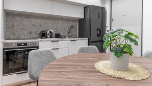 A modern kitchen with white cabinets, a stainless steel refrigerator, and a dining table with chairs. - Phaedrus Living: Prosperity Residences Paradise (Athina)