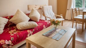 Ein Zimmer mit einem blumigen Sofa, einem Holztisch mit einer Vase und Blick auf Grün.