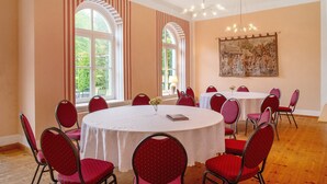 Ein Konferenzraum mit rundem Tisch, roten Stühlen, großen Fenstern und einer Kristallleuchtre.