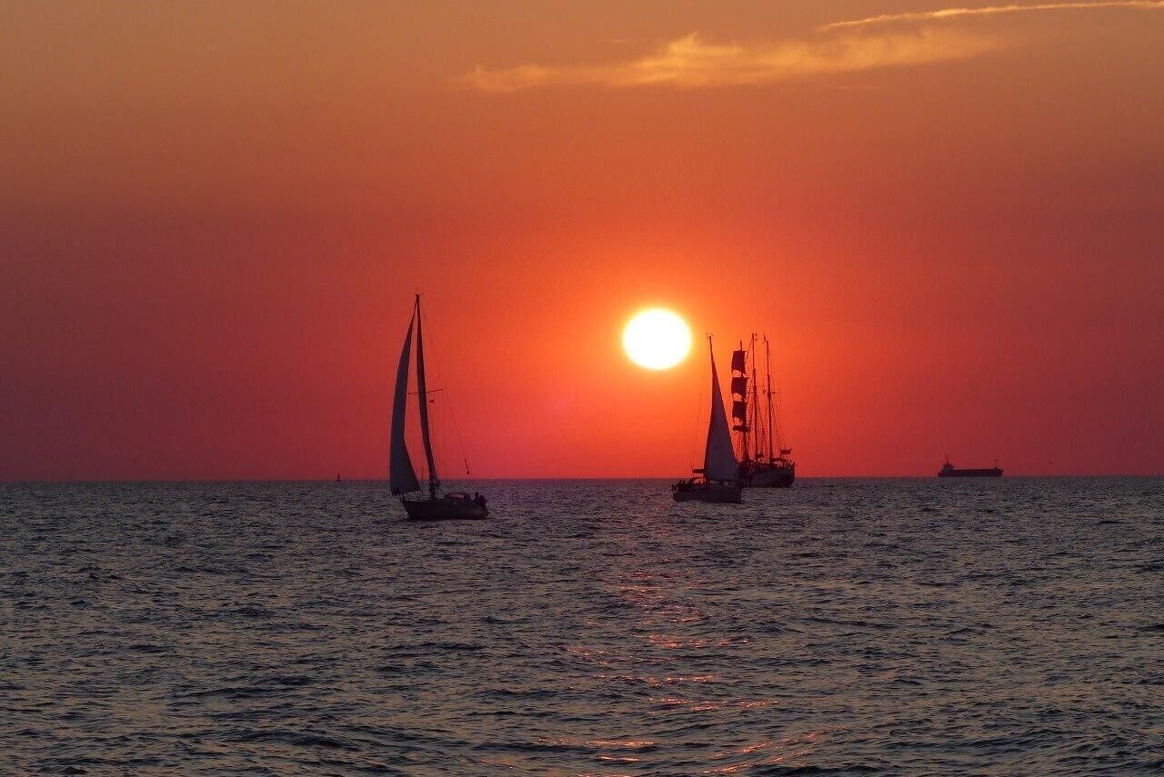A sunset over the ocean with sailboats.