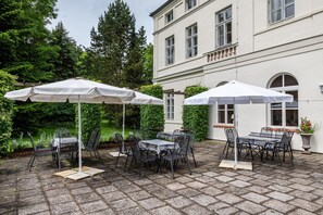 A patio area with tables and chairs, white umbrellas, and a building with arched windows and a balcony. - Apartment 'Ferienwohnung 8' with Shared Terrace and Shared Garden (Krakow am See)
